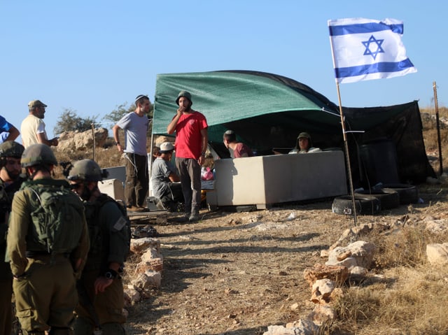 Soldaten und junge Menschen bei einem Zelt in der Wüste. Daneben eine israelische Flagge