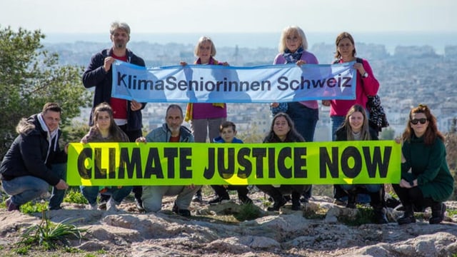 Seniorinnen und junge Aktivist:innen halten zwei Banner vor Stadtlandschaft