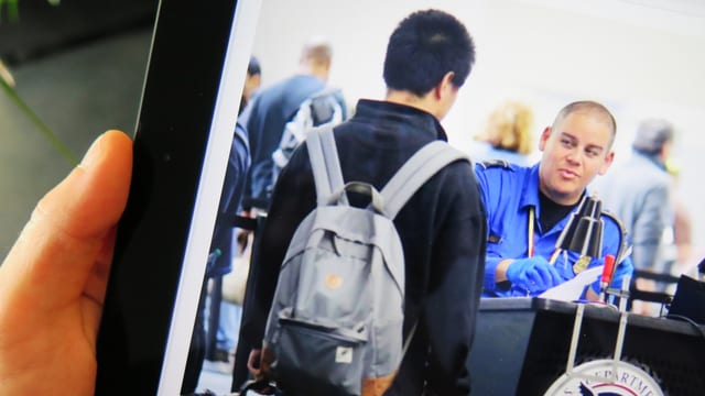 Ein Tablet, das ein Foto von einer Zollkontrolle am Flughafen zeigt.