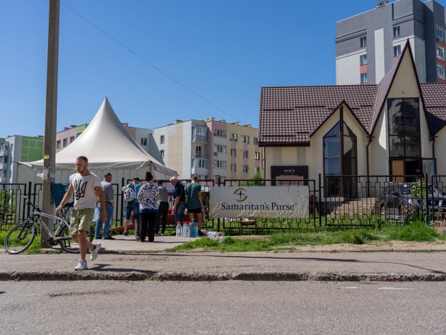 Menschen versammeln sich unter einem Zelt vor einem Gebäude mit einem Samaritan's Purse Schild.