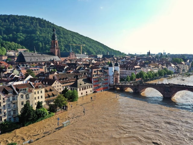 Überflutete Altstadt mit Fluss, Brücke und Kirche im Hintergrund.