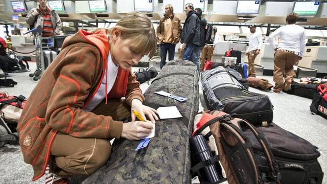 Snowboarderin mit ihrem Spezialgepäck am Flughafen-Check-In