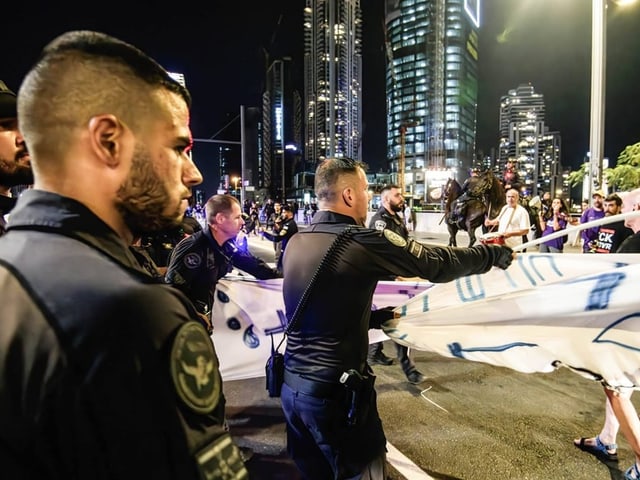 Polizisten entfernen Banner bei Nachtprotest in Stadt.