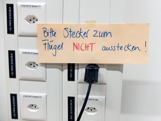 Kleber «Bitte Stecker zum Flügel nicht ausstecken!» auf Stromleiste.