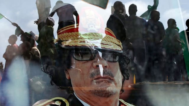 Der gestürzte Diktator Gaddafi, im Hintergrund Flüchtlinge. 