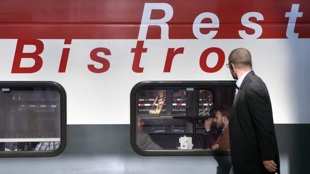 Mann steht vor Bistro-Zugfenster mit Menschen im Inneren.