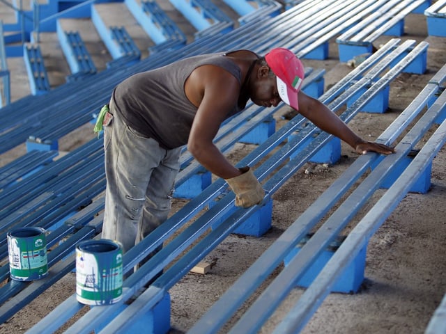 Ein Arbeiter streicht die Sitzbänke im Stadion mit blauer Farbe an.