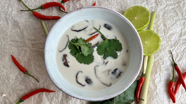 Tom Kha Gai-Suppe in einer weissen Suppenschale. Dekoriert mit roten Chili, Limetten, Koriander und Zitronengras.