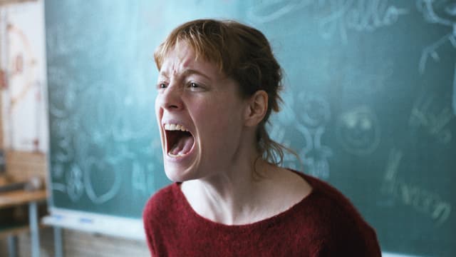 Eine Frau steht vor einer Wandtafel und schreit aus voller Kehle.