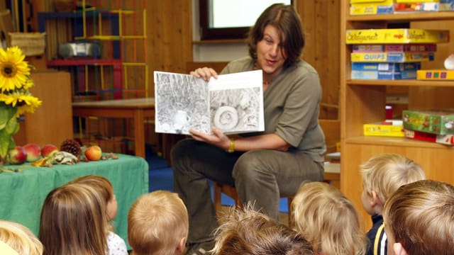 Eine Frau liest Kindern aus einem Buch vor.