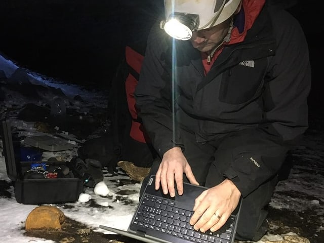 Lütscher auf den Knien in der Höhe. Er tippt auf seinem Laptop. 