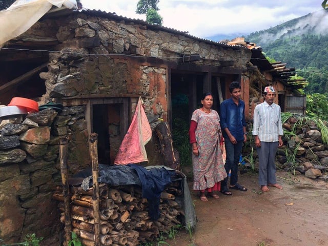 Die Familie mit Mutter, Vater und Sohn steht vor den übrig gebliebenen Mauern ihres Hauses.