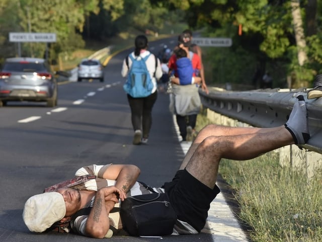 Ein Migrant liegt auf einer Strasse und schläft. Sein Gesicht wird von einer Mütze verdeckt.