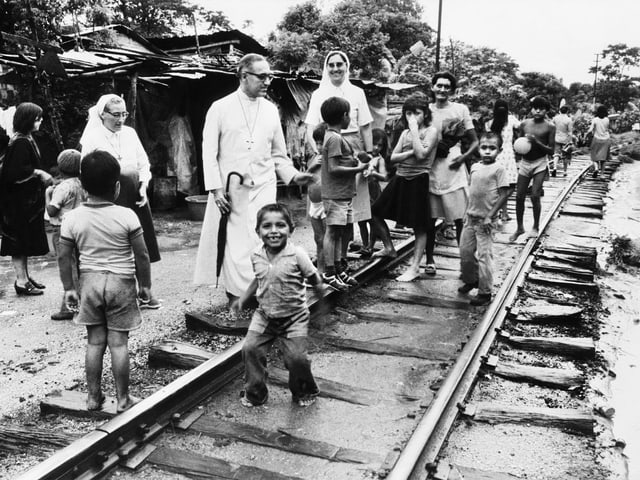 Priester Romero und zwei Nonnen besuchen Kinder und Frauen, die in El Salvador in Baracken leben