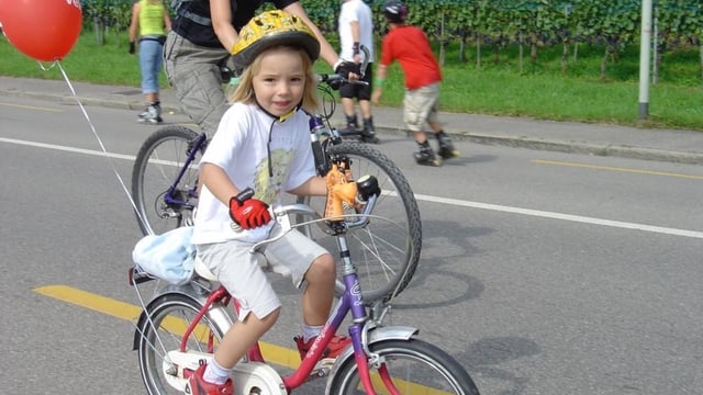 Ein Kind fährt auf dem Fahrrad auf einer Strasse. 