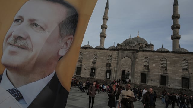 Ein Erdogan-Plakat vor einer Moschee in der Türkei, Menschen auf dem Vorplatz.