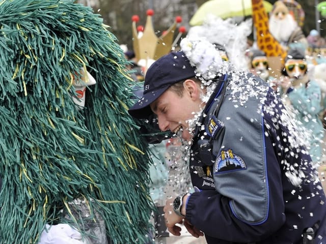 Polizist bekommt Räppli in die Uniform gestopft von einer Person im Fasnachtskostüm.