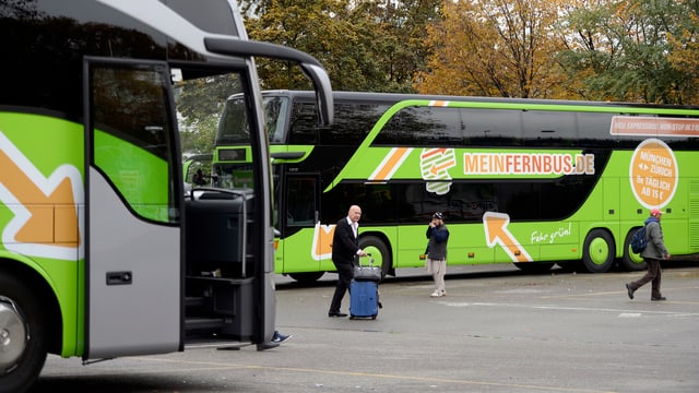 Zwei parkierte Fernbusse, einige Personen schlendern vorbei.