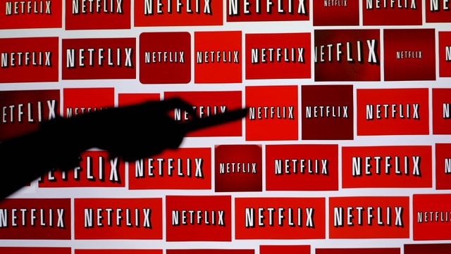 A hand with a remote control in front of Netflix logos