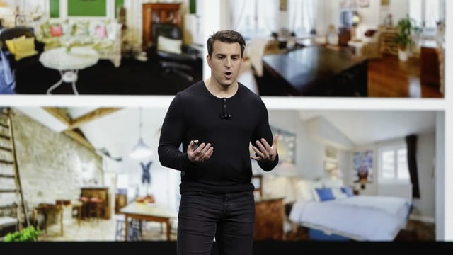 Brian Chesky in front of a canvas with representations of rooms.