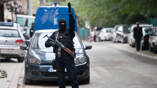 Schwer bewaffneter, schwarz gekleideter Polizist seht auf der Strasse.