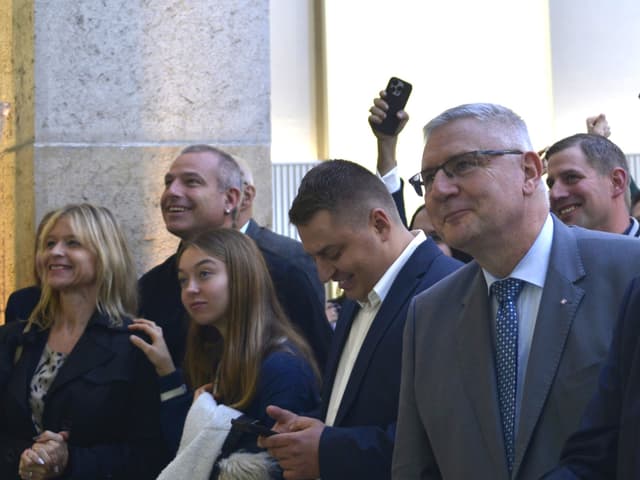 Gruppe von Menschen in formeller Kleidung lächelt und schaut nach vorne.