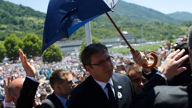 Serbiens Ministerpräsident Alexandar Vucic wird mit einem Schirm vor Angriffen geschützt.