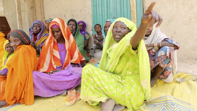 In farbige Tücher gekleidete Frauen sitzen in einem Hof in Damask, Nigeria.