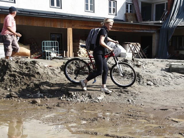 Eine Frau stösst ihr Velo. Rund um sie sind viel Geröll und braune Wasserpfützen zu sehen.