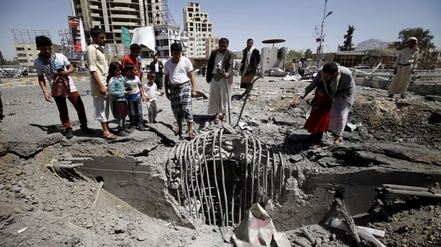 Menschen stehen um dein Einschlagsort einer Bombe in der jemenitischen Hauptstadt Sanaa.