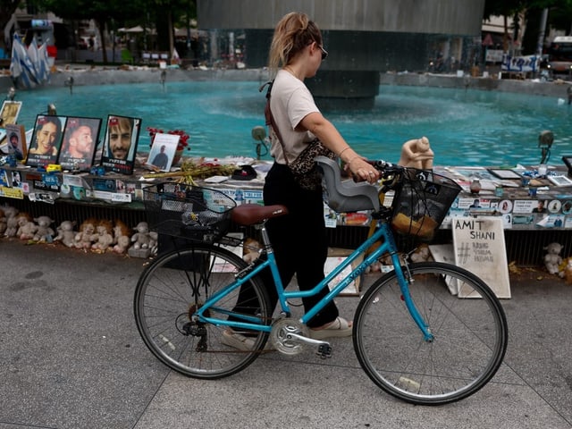 Frau mit Fahrrad vor Brunnen mit Fotos und Gedenktafeln.