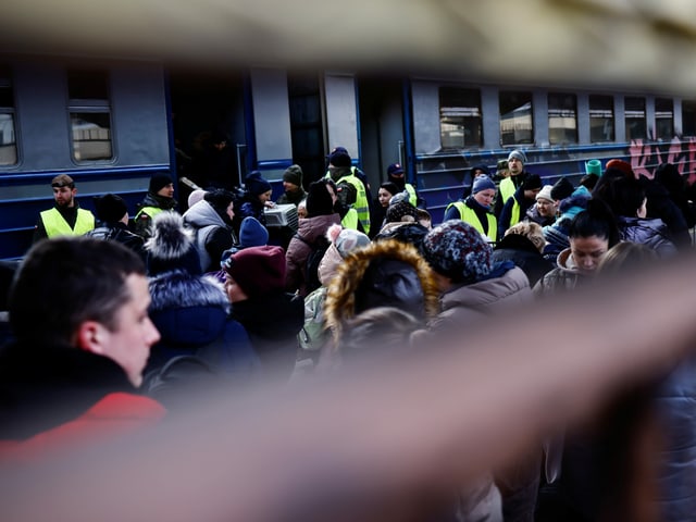 Menschen stehen vor einem blauen Zug. Es hat Wärter in Leuchtwesten.