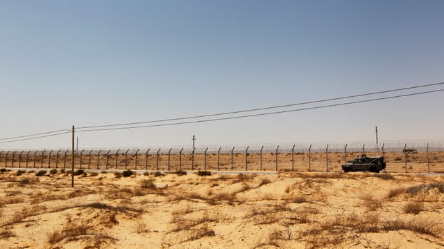 Ein Fahrzeug fährt einen Grenzzaun entlang, dahinter die Wüste Sinai.