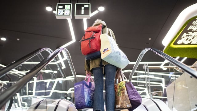 Frau auf Rolltreppe von hinten mit Einkaufstüten