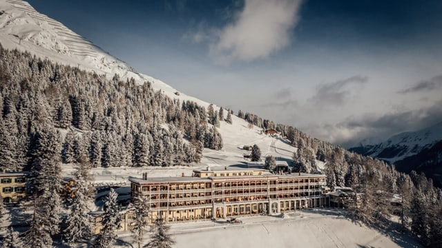 Ein riesiges, altes, längliches Hotelgebäude am Berg in einem verschneiten Wald.