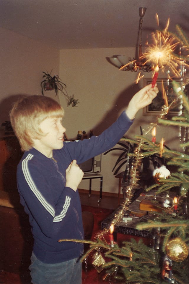 Junge zündet Kerze an Weihnachtsbaum an und trägt dunkelblauen Trainer. 