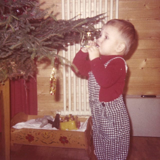 Ein kleiner Bub mit rotem Pullover und karierter Hose nascht Schokolade von einem Weihnachtsbaum.