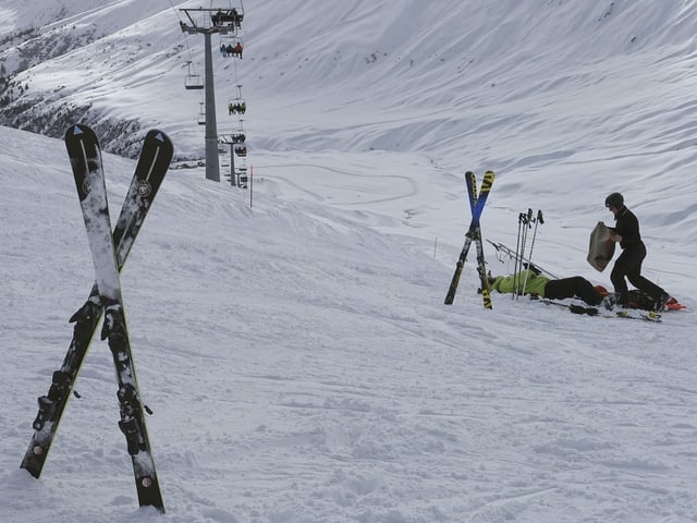 Ein Mann kümmert sich um einen Skifahrer der am Boden liegt.