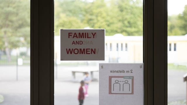 Schilder an einem Fenster mit der Aufschrift 'Family and Women' und '2 m distance.'