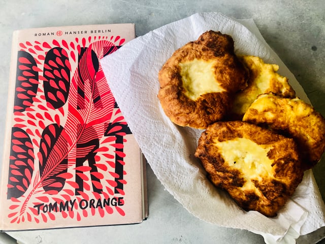 Neben dem Roman «Dort Dort» von Tommy Orange steht ein Teller mit selbstgemachtem Fry Bread. 