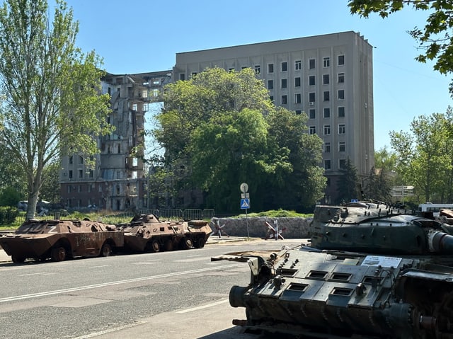 Zerstörte Militärfahrzeuge vor einem beschädigten Gebäude.