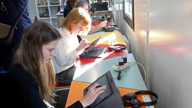 Vier Mädchen sitzen nebeneinander, vor ihnen Tablets und Laptops. Die Sonne scheint durchs Fenster.