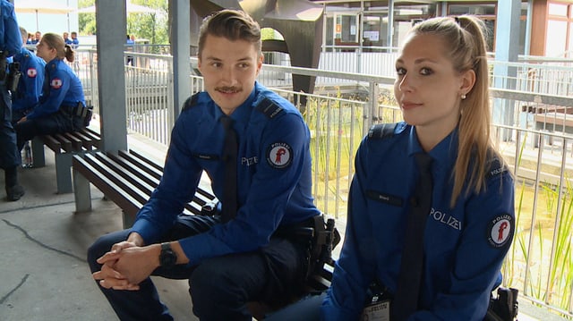 Ein junger Mann und eine junge Frau in Polizeiuniform sitzen auf einer Bank.