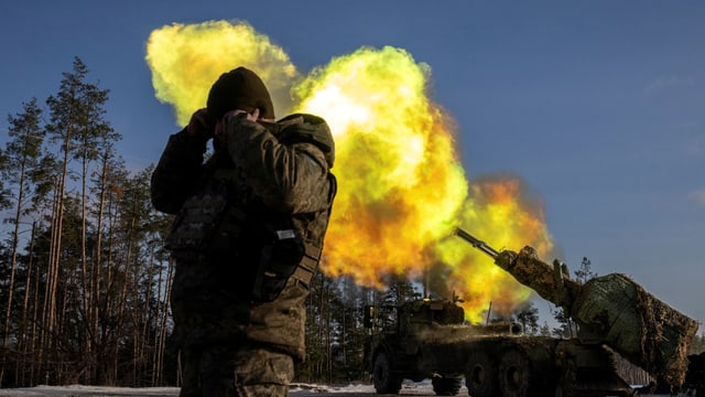 Artilleriegeschütz feuert, Soldat hält sich die Ohren zu.