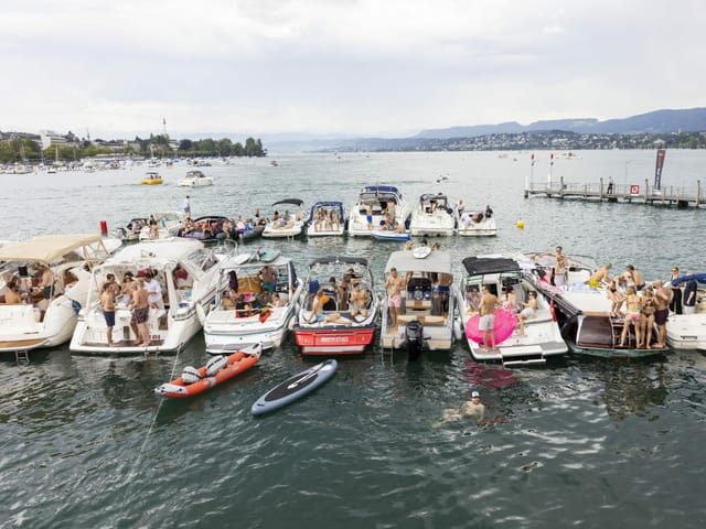 Mehrere Boote liegen aneinandergereiht im Zürcher Seebecken. Auf den Booten tummeln sich Leute.