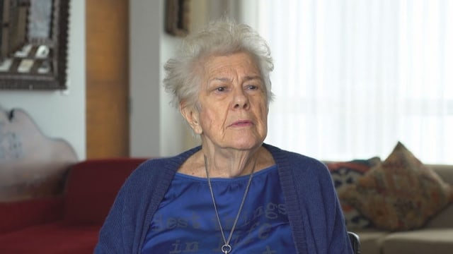 Die 88-jährige Esther mit kurzen weissgrauen Haaren, leicht geschminkt, sitzt auf einem Sofa und erzählt.