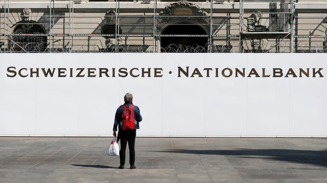 Ein Mann mit rotem Ruckstack steht vor dem Nationalbank-Gebäude.