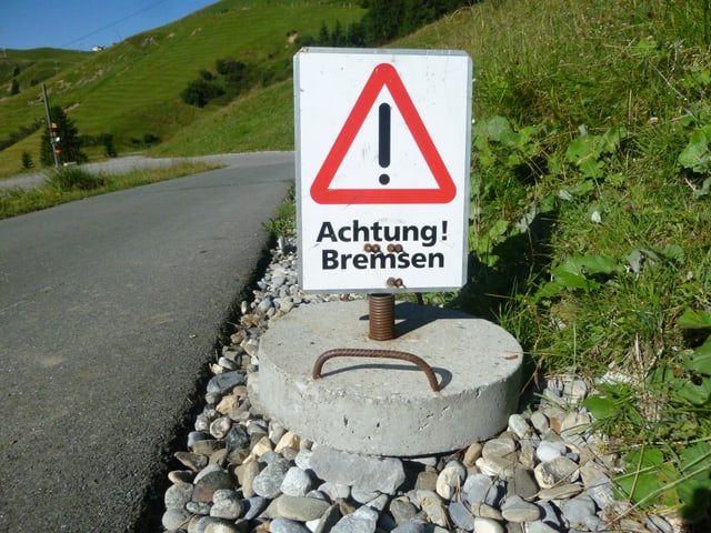 Vor einer Kurve steht eine Warntafel «Achtung Bremsen»