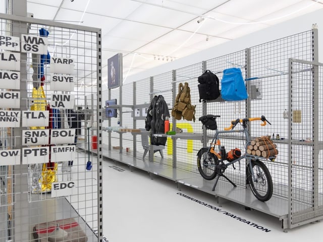 Fahrrad mit Gepäck an Gitterwand in Ausstellung.