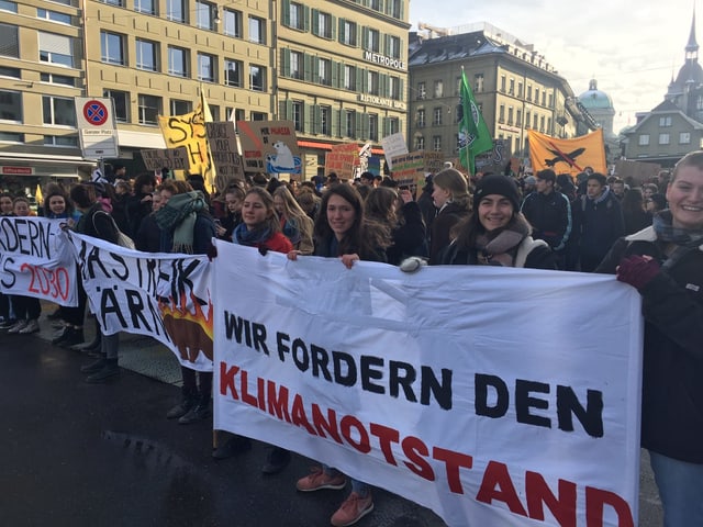 Menschenmenge auf grossem Platz. Schülerinnen halten Transparent: «Wir forden den Klimanotstand».